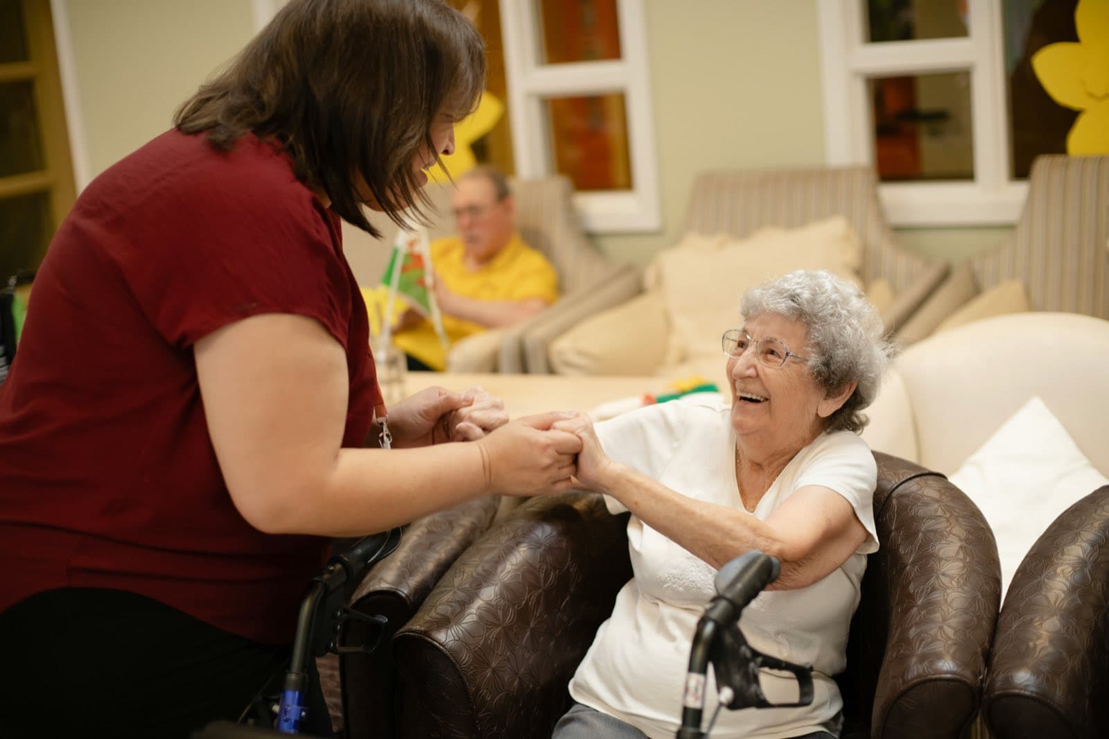 A caregiver holding the hands of a smiling resident in an armchair.