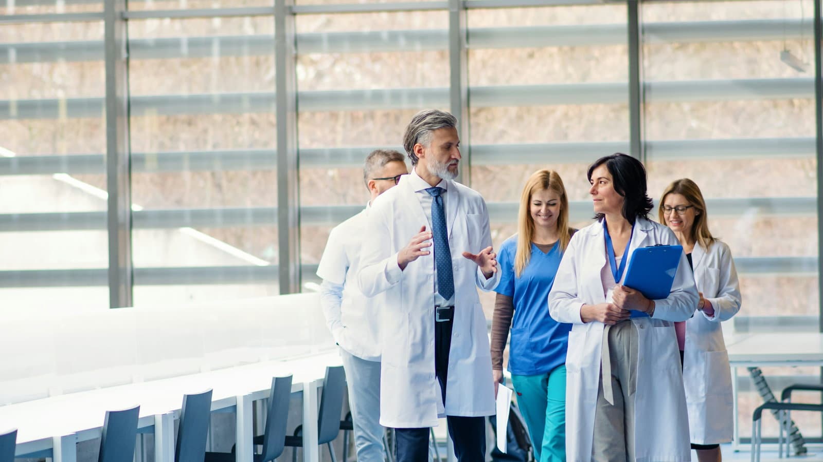 Four clinicians in white coats and scrubs walking and talking.