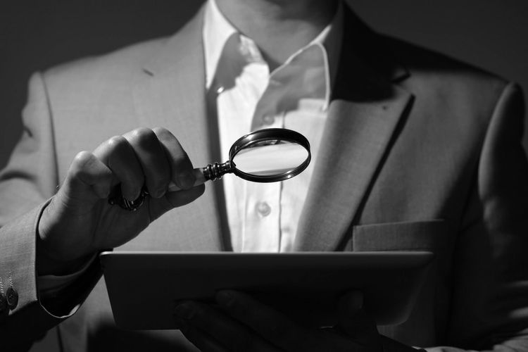 Suited man holding a magnifying glass over a document.